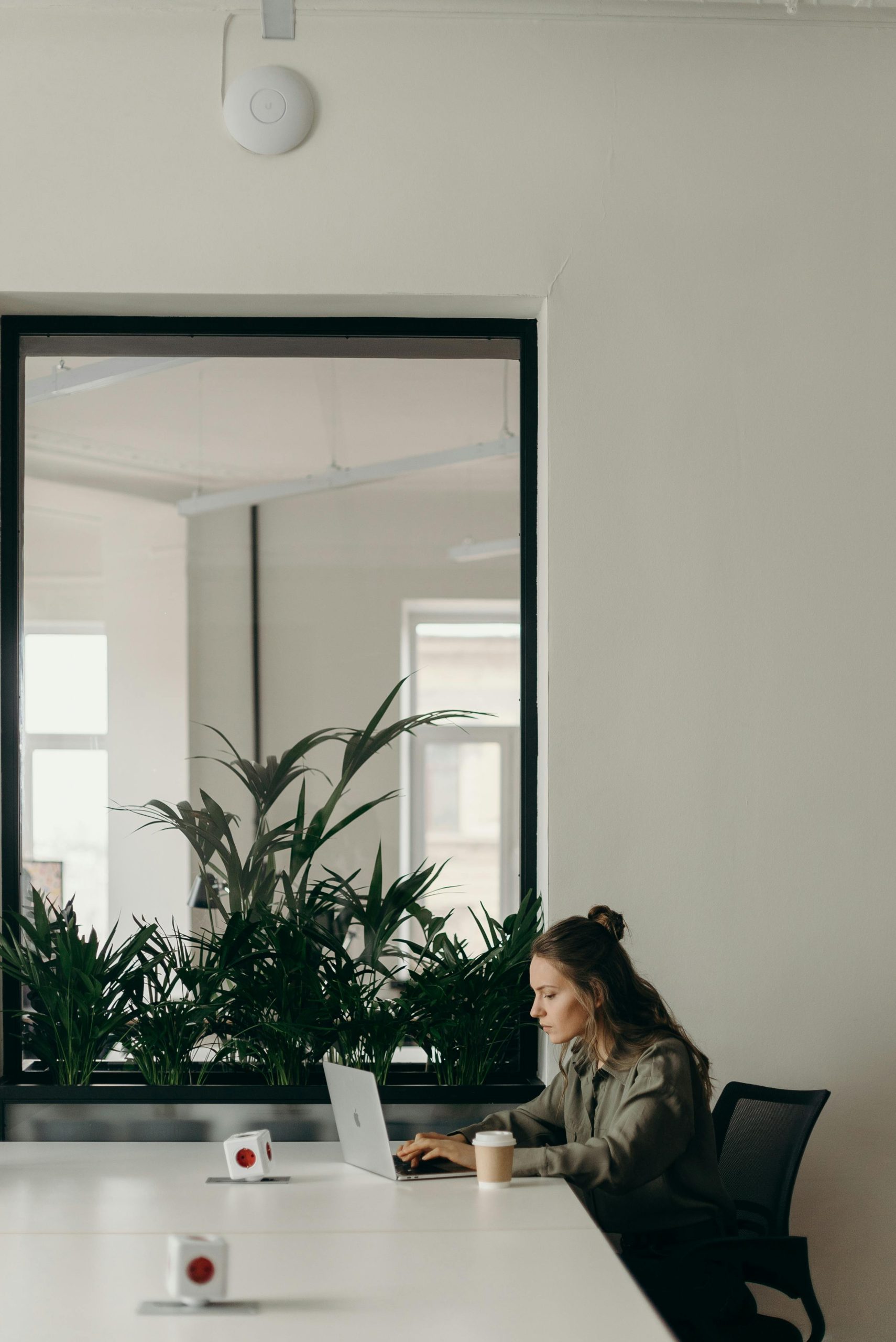 Woman working on a laptop in a minimalist home office with plants.