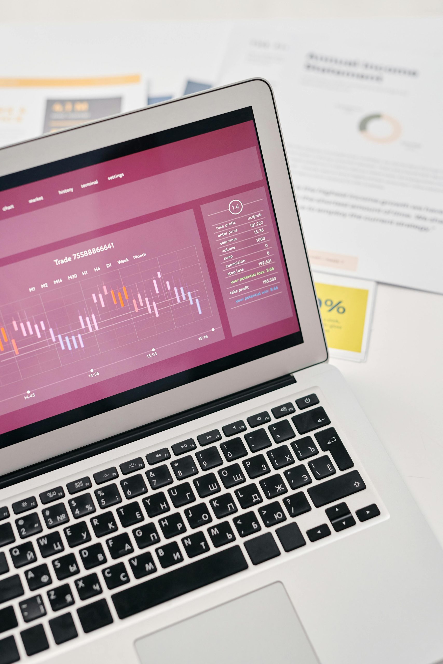 High angle view of a laptop displaying financial graphs and analytics alongside printed documents and reports.